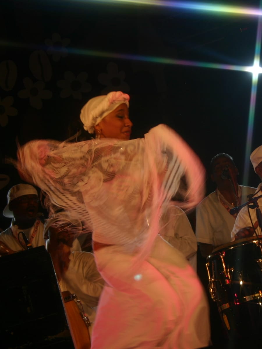 A bomba dancer in white swirls her skirt as drummers play behind her in Guaynabo, Puerto Rico